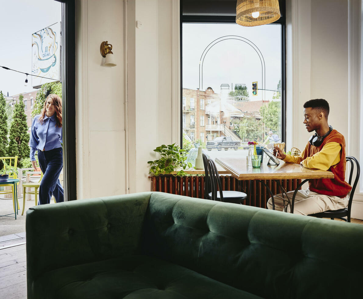 Female entering a cafe, male sitting at a table with headphones working on a tablet with a touch pen